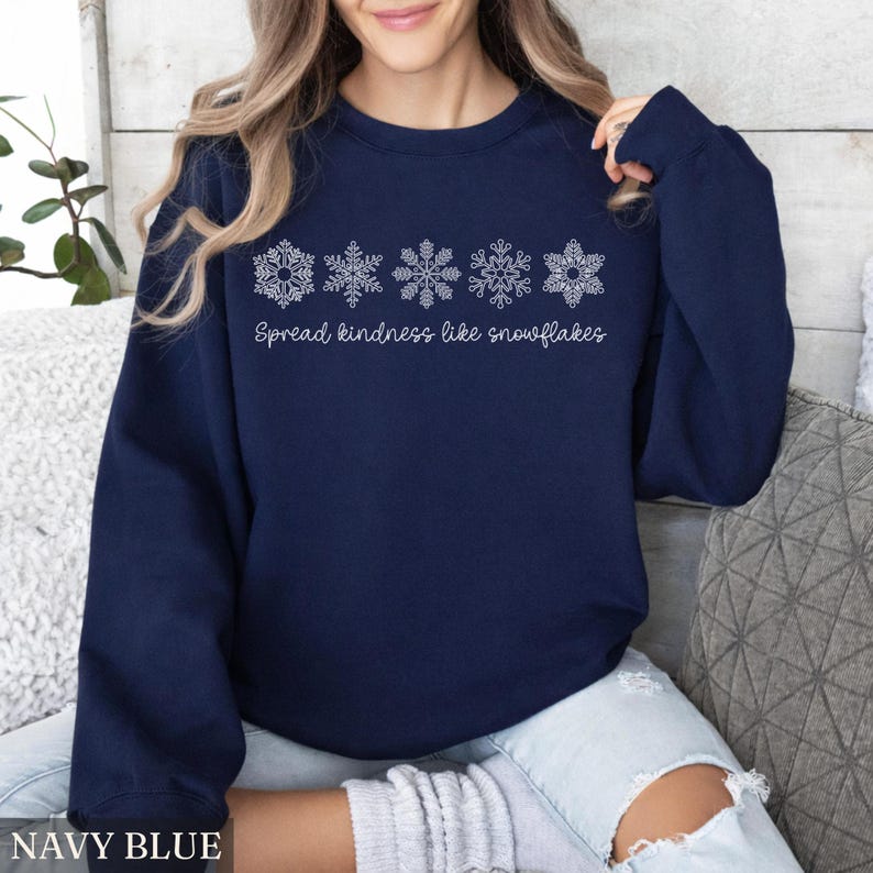 May include: Navy blue sweatshirt with white snowflake designs and the text "Spread kindness like snowflakes." The sweatshirt is a solid navy blue color. The words "NAVY BLUE" are at the bottom of the image.