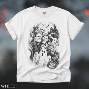 May include: A white t-shirt featuring a black and white graphic print of classic horror movie monsters including Frankenstein, Dracula, a mummy, a ghost, and a werewolf, with a haunted castle and full moon in the background and a jack-o'-lantern.