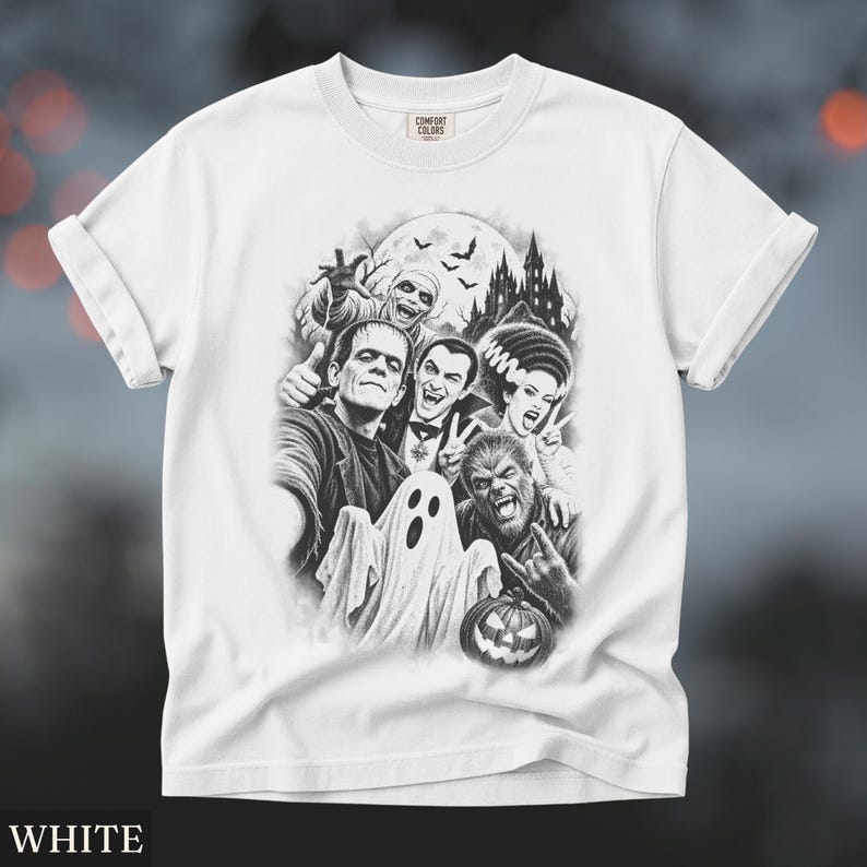May include: A white t-shirt featuring a black and white graphic print of classic horror movie monsters including Frankenstein, Dracula, a mummy, a ghost, and a werewolf, with a haunted castle and full moon in the background and a jack-o'-lantern.