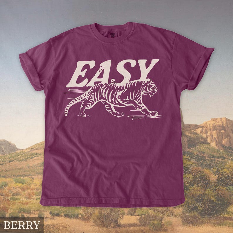 Op de afbeelding: Bessenkleurig T-shirt met het woord "EASY" in grote, witte blokletters boven een witte tijgerillustratie. De tijger loopt, met zijn strepen zichtbaar. Het shirt heeft korte mouwen en een ronde hals.