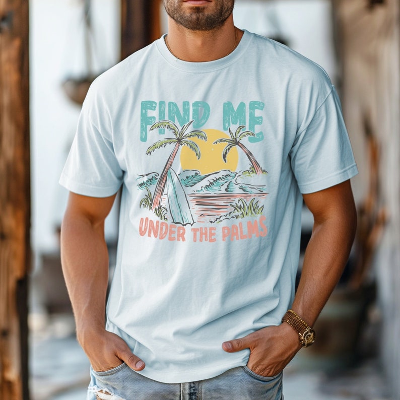 May include: A light blue t-shirt with a graphic print of palm trees, waves, and a surfboard. The text "Find Me Under The Palms" is printed on the shirt.