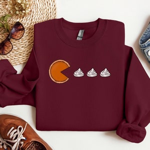 Pode incluir: Uma camisa de moletom vinho com um gr&aacute;fico de uma fatia de torta de ab&oacute;bora com uma mordida, perseguindo tr&ecirc;s mini marshmallows.