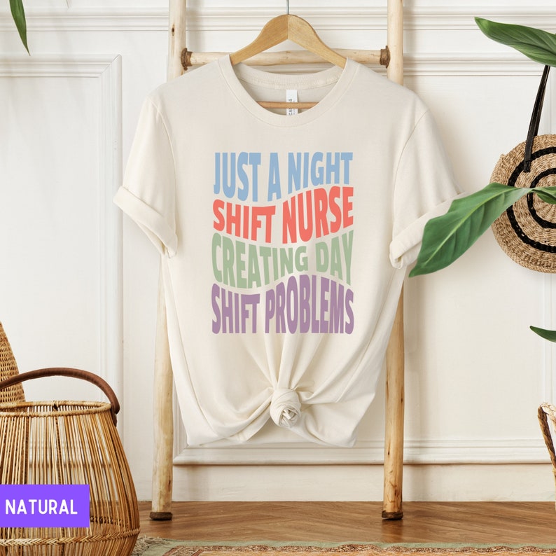 May include: A white t-shirt with the text "Just a night shift nurse creating day shift problems" in rainbow colours.