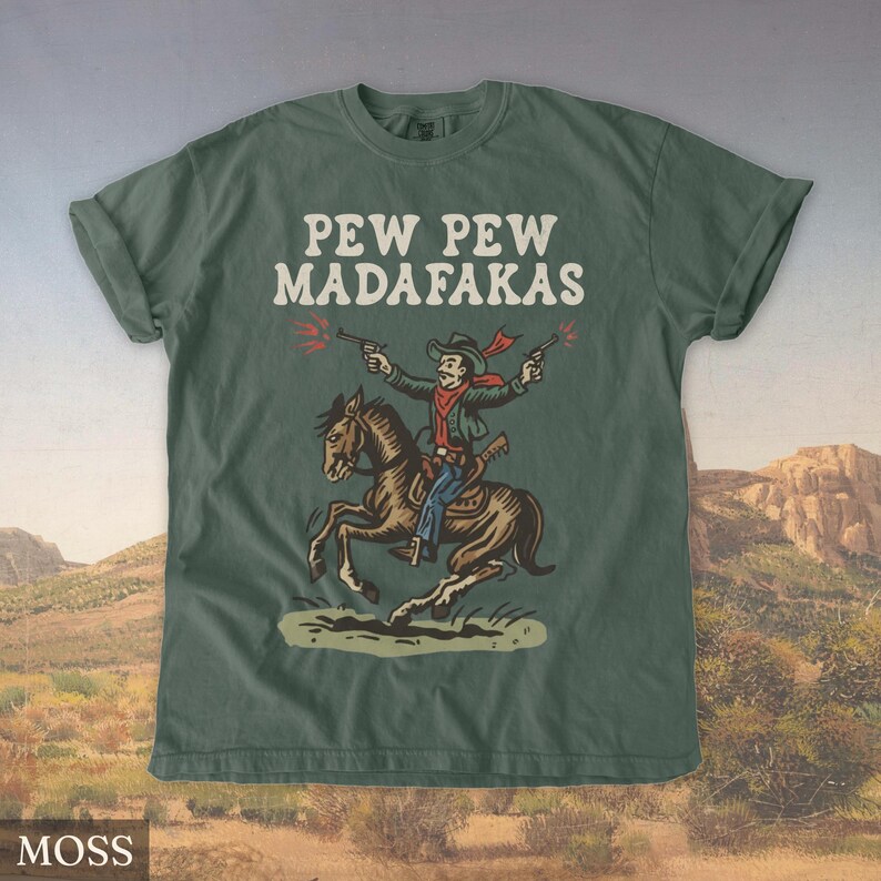 Puede incluir: Camiseta verde musgo con el texto "PEW PEW MADAFAKAS" sobre un vaquero de dibujos animados montado a caballo y disparando pistolas. El vaquero lleva una bufanda y un sombrero rojos. El caballo es marr&oacute;n.