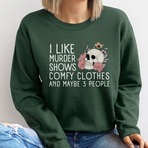 Op de afbeelding: Een donkergroen sweatshirt met de tekst "Ik hou van moordshows, comfortabele kleding en misschien 3 mensen" en een schedel met bloemen.