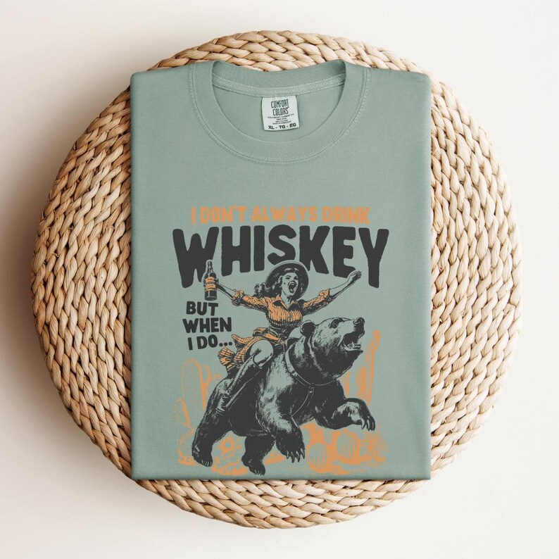 May include: A green t-shirt with the text "I don't always drink whiskey, but when I do..." and a graphic of a woman riding a bear while holding a bottle of whiskey.