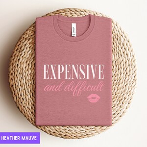 May include: Heather mauve t-shirt with the text "EXPENSIVE and difficult" in white and a pink lip print.
