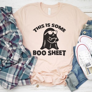 May include: A pink t-shirt with a black graphic of a ghost wearing sunglasses and the text "This is some boo sheet".