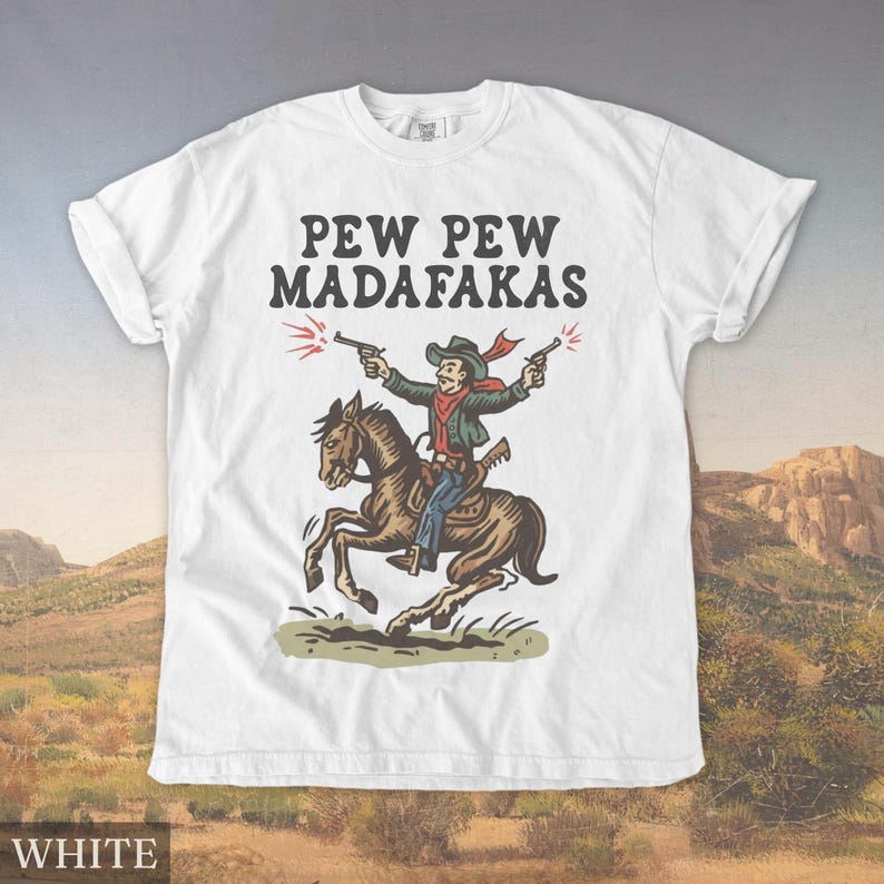 Puede incluir: Camiseta blanca con un dise&ntilde;o de un vaquero a caballo disparando dos pistolas. El texto "PEW PEW MADAF*KAS" est&aacute; impreso encima de la ilustraci&oacute;n. La palabra "WHITE" est&aacute; impresa en la parte inferior.
