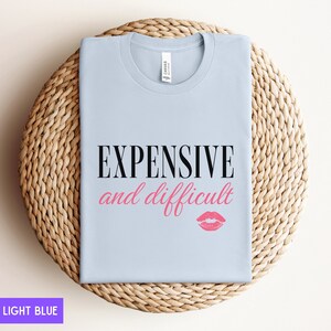 May include: Light blue t-shirt with the text "EXPENSIVE and difficult" in black and a pink lipstick print.