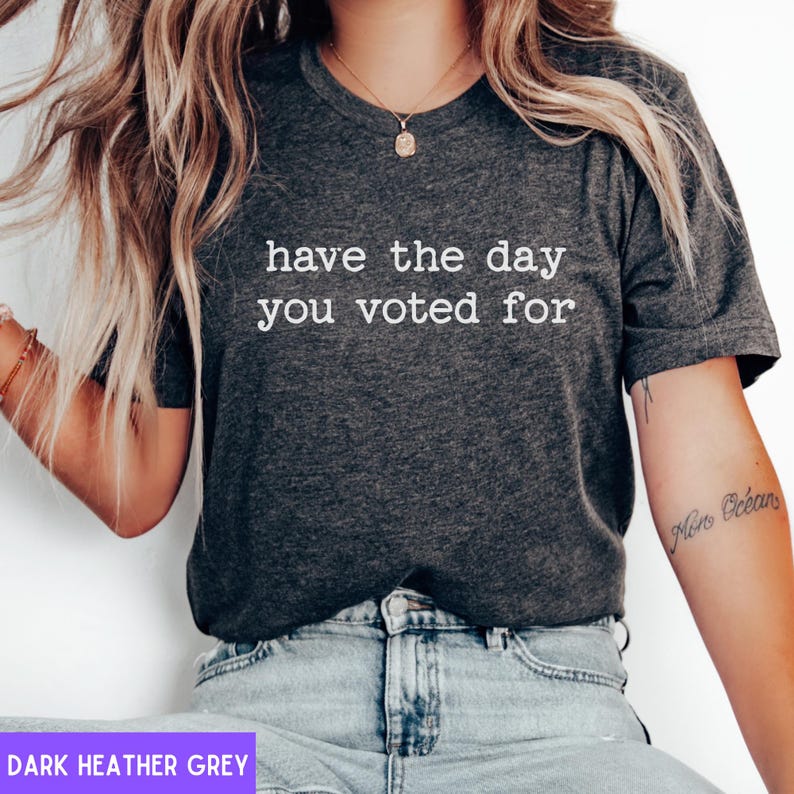 May include: A dark heather grey t-shirt with the text "have the day you voted for" printed in white.
