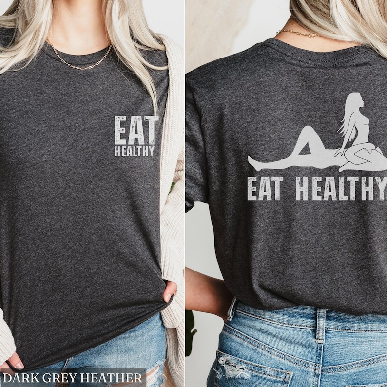 May include: Dark grey heather t-shirt with the text "EAT HEALTHY" printed on the front and back. The back of the shirt features a graphic of a person reclining with the same text. The shirt is a crew neck.