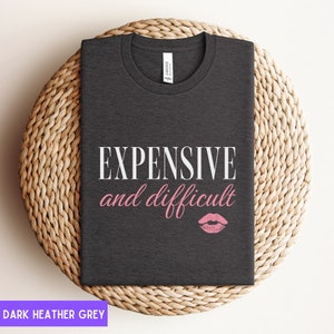 May include: Dark heather grey t-shirt with the text "EXPENSIVE and difficult" in white and a pink lipstick print.