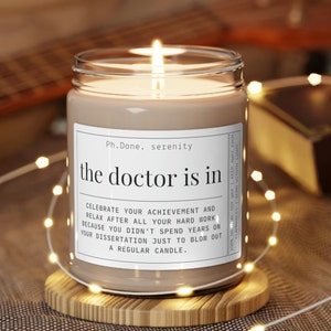 May include: A brown candle with a white label that reads "Ph.Done. serenity the doctor is in CELEBRATE YOUR ACHIEVEMENT AND RELAX AFTER ALL YOUR HARD WORK BECAUSE YOU DIDN'T SPEND YEARS ON YOUR DISSERTATION JUST TO BLOW OUT A REGULAR CANDLE."