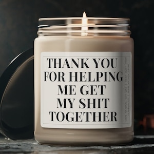May include: A brown soy candle with a white label that reads "Thank you for helping me get my shit together".