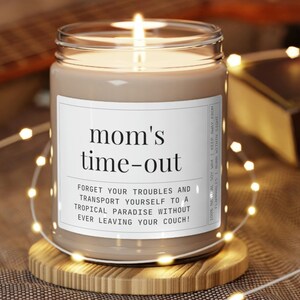 May include: A brown glass candle with a white label that reads "mom's time-out" and "Forget your troubles and transport yourself to a tropical paradise without ever leaving your couch!"