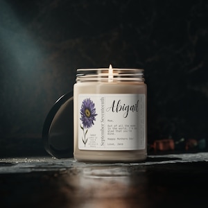 May include: A beige candle with a white label featuring a purple aster flower and the text "September Seventeenth", "Abigail", "Mom, Out of all the moms in the world, I'm so glad that you're mine. Happy Mothers Day! Love, Jane".