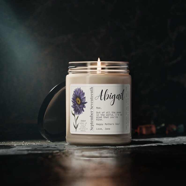 May include: A beige candle with a white label featuring a purple aster flower and the text "September Seventeenth", "Abigail", "Mom, Out of all the moms in the world, I'm so glad that you're mine. Happy Mothers Day! Love, Jane".