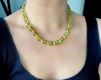 May include: A green gemstone necklace with gold accents. The necklace is made of round beads and is worn by a person.