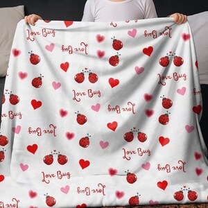 May include: White blanket with a repeating pattern of red ladybugs, red and pink hearts, and the words "Love Bug" in red script. The blanket is soft and cozy, perfect for snuggling up on the couch.