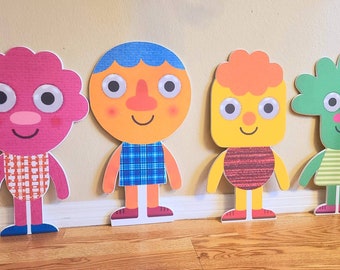 May include: Four colorful felt cutouts of cartoon characters with large eyes and smiling faces. The characters are standing in a row on a wooden floor.