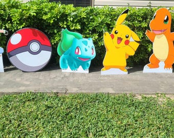 May include: Five cardboard cutouts of Pokemon characters. The characters are Pikachu, Bulbasaur, Charmander, Squirtle, and a Pokeball. The cutouts are on a green lawn in front of a brick wall.