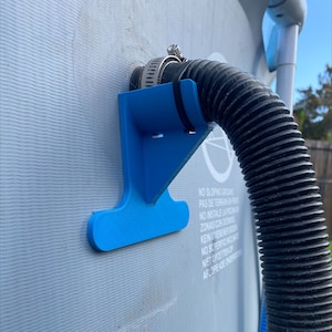 May include: A blue plastic hose holder attached to a pool wall. The holder has a black hose attached to it with a silver clamp.