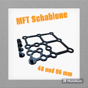 Può includere: Modello in plastica nera con fori disposti a griglia. Il modello è etichettato "MFT Schablone" e "48 und 96 mm".