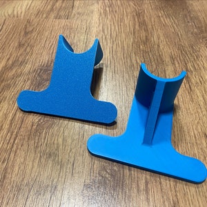 May include: Two blue plastic stands for holding items, such as a phone or tablet, on a wooden surface.