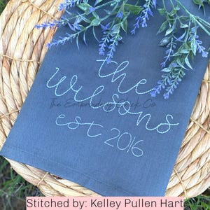 Puede incluir: Una toalla de té gris con bordado blanco que dice "The Wilsons est 2016".