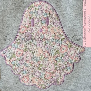 May include: A purple ghost applique with a floral pattern on a gray sweatshirt. The ghost has a simple face with two eyes and a mouth. The text "Stitched by @bellesandbuds_monograms" is in the upper right corner of the image.