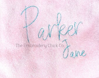May include: Pink fabric with the name "Parker Jane" embroidered in turquoise thread. The text "The Embroidery Chick Co." is also embroidered below the name.
