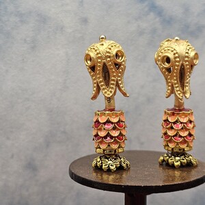 May include: Two ornate, gold-colored decorative objects with an octopus-like design on top. The lower portion features a layered, scale-like pattern in shades of pink and red. They sit on a small, round, dark brown table.