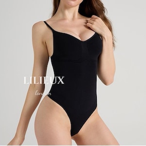 Puede incluir: Body negro con tirantes finos y escote corazón. La prenda tiene una silueta ajustada y una parte trasera de tanga. El texto "LILIEUX London" está impreso en blanco en la parte delantera del body.