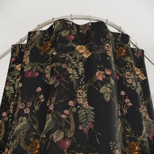 May include: A black shower curtain featuring a detailed botanical print of winding tree branches, blooming flowers in shades of orange and pink, small mushrooms, and dark red fruits, suspended from a curved metal rod with silver shower rings.