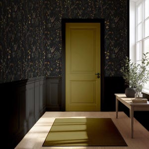 K&ouml;nnte beinhalten: Innenaufnahme mit einer senffarbenen T&uuml;r und schwarzem Rahmen, vor floraler Tapete. Ein kleiner Holztisch tr&auml;gt eine Topfpflanze. Der Raum hat einen Teppich und Holzb&ouml;den.