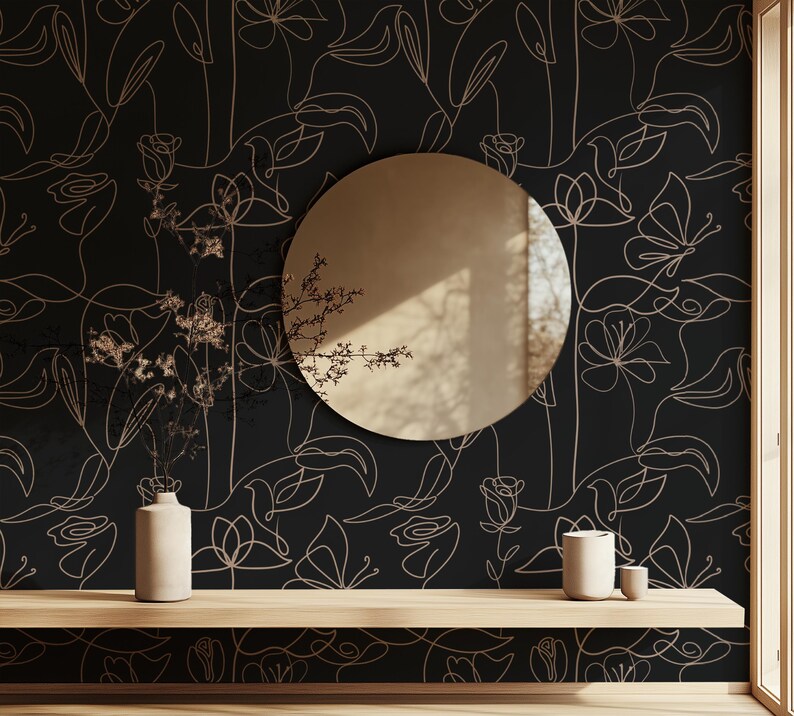 Puede incluir: Un papel tapiz negro y dorado con un dise&ntilde;o floral minimalista. El papel tapiz presenta delicados dibujos lineales de flores y hojas. Un espejo redondo y dos jarrones de cer&aacute;mica se colocan en un estante de madera frente al papel tapiz.