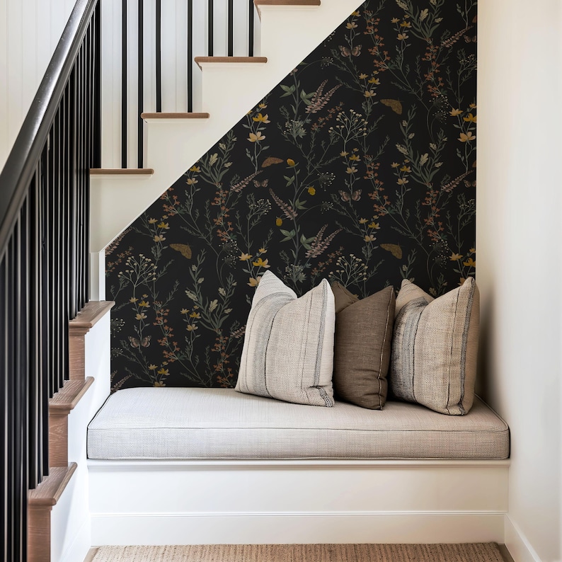 K&ouml;nnte beinhalten: Eine gem&uuml;tliche Sitzbank mit drei dekorativen Kissen befindet sich unter einer Treppe. Die Wand hinter der Bank ist mit einer dunklen floralen Tapete verziert. Die Treppe hat ein schwarzes Gel&auml;nder und Holzstufen.