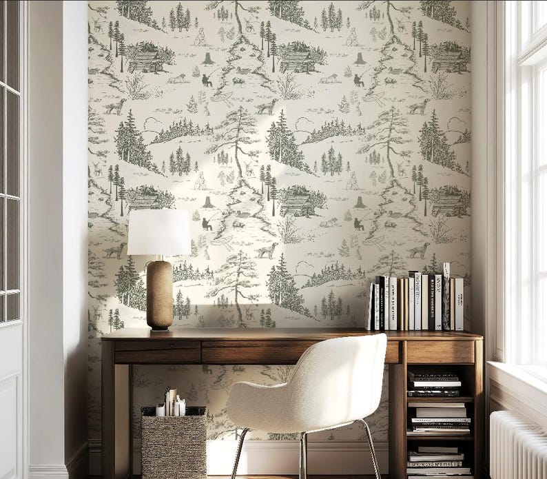 May include: A home office with a wooden desk, a white chair, and a lamp. The wall is covered in a cream-colored wallpaper with a black and white forest scene. Books are on the desk and in a shelf below.