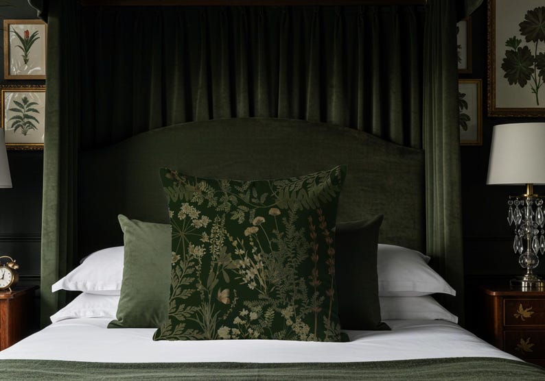May include: A dark green bed with a velvet headboard and matching curtains. The bed is made with white sheets and several pillows. The pillows include a floral patterned pillow and two solid green pillows. A lamp and framed botanical prints are visible.
