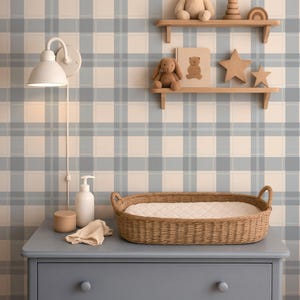 Peut inclure: Intérieur de chambre d'enfant avec une commode bleue, un panier à langer en osier et des étagères avec des jouets. Le fond est un papier peint à carreaux bleu et blanc. Une lampe murale blanche est présente.