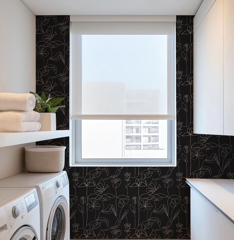 Puede incluir: Un papel tapiz floral blanco y negro con un delicado dise&ntilde;o de l&iacute;neas. El papel tapiz presenta un patr&oacute;n repetitivo de flores y hojas en un estilo minimalista. El papel tapiz se muestra en un ba&ntilde;o con una lavadora blanca y una ventana con vista a una ciudad.