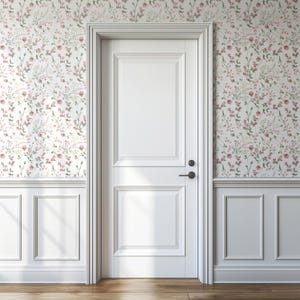 Op de afbeelding: Een witte binnendeur met zwart beslag staat centraal in de afbeelding. De deur wordt omgeven door witte panelen en bloemenbehang in roze, groen en wit. De vloer is van hout.