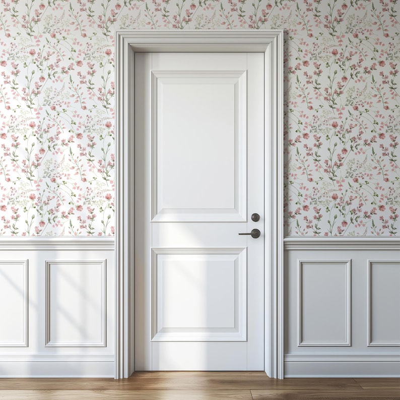 Op de afbeelding: Een witte binnendeur met zwart beslag staat centraal in de afbeelding. De deur wordt omgeven door witte panelen en bloemenbehang in roze, groen en wit. De vloer is van hout.