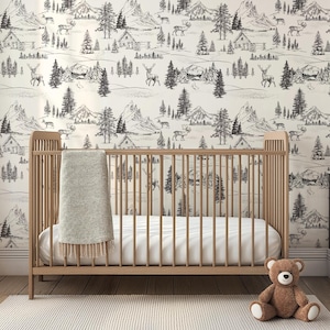 Puede incluir: Una cuna de madera clara con un colch&oacute;n blanco y una manta gris. La cuna est&aacute; frente a una pared con un papel pintado con un paisaje de monta&ntilde;a y bosque en blanco y negro. Un oso de peluche marr&oacute;n est&aacute; en el suelo.