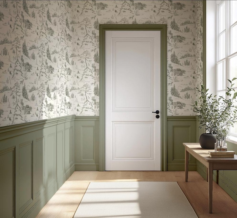 May include: A room with a white door, green trim, and wallpaper featuring a forest scene. A wooden table holds a plant and books. The room has a window and a light-colored rug.