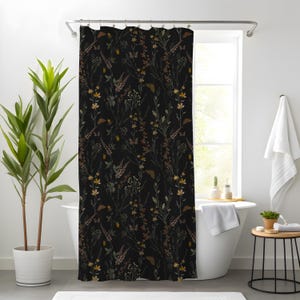 May include: A black shower curtain with a botanical pattern. The design features various wildflowers and foliage in shades of yellow, brown, and green. The curtain is hanging in front of a white bathtub, creating a nature-inspired bathroom theme.