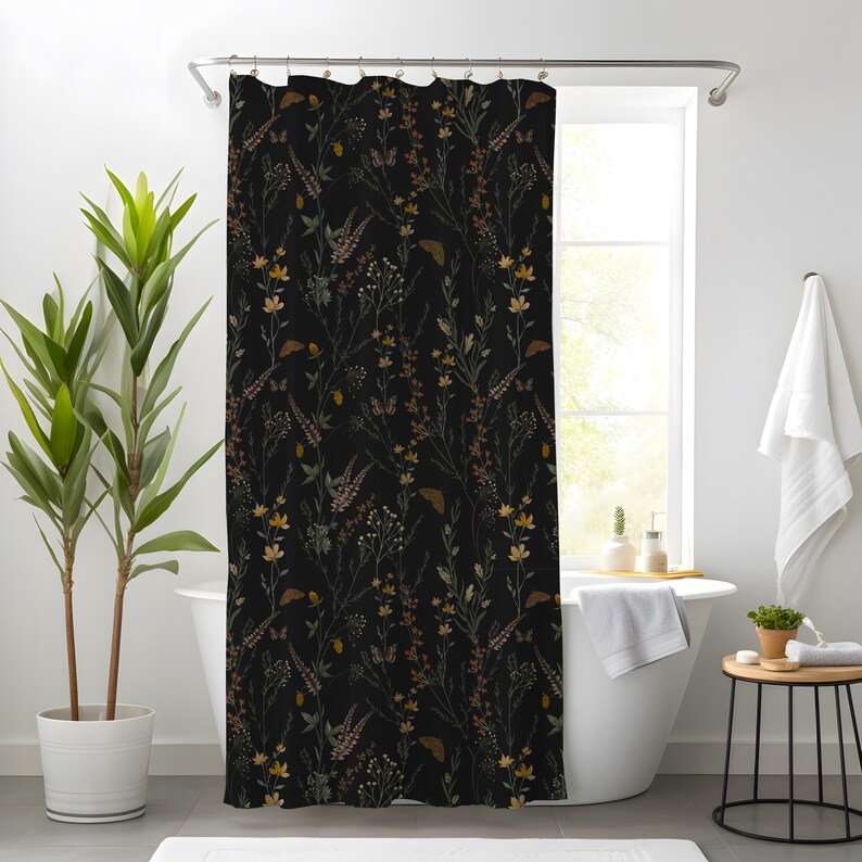 May include: A black shower curtain with a botanical pattern. The design features various wildflowers and foliage in shades of yellow, brown, and green. The curtain is hanging in front of a white bathtub, creating a nature-inspired bathroom theme.