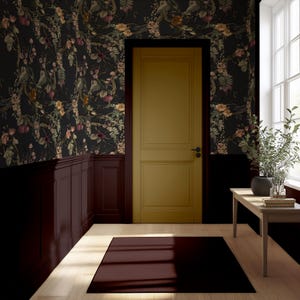 May include: Interior scene featuring a mustard-colored door, dark floral wallpaper, and a burgundy rug. The walls are painted in dark colors, with a wooden paneling. A small wooden table holds a plant and books, and a window provides natural light.