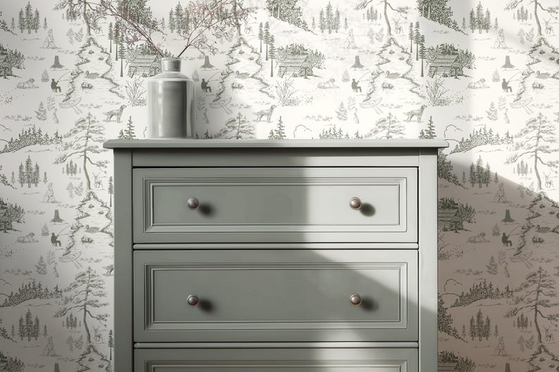 May include: A gray dresser with three drawers and silver knobs. A gray vase with branches sits on top of the dresser. The background features a black and white forest-themed wallpaper.
